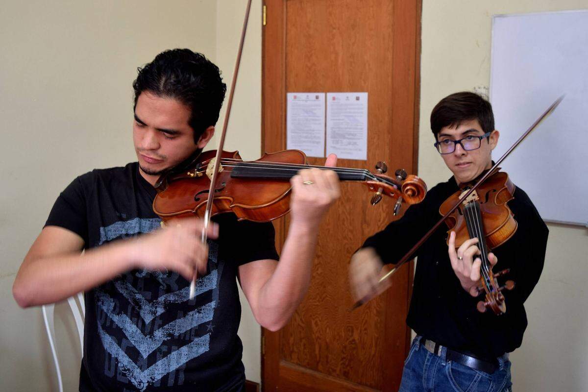 Pedro Changir (izq) y Zabdiel Hernández ensayan antes de una clase de música en Lima, Perú. Los dos jóvenes estudieron en el famoso programa venezolano de música clásica y acreditan a esa experiencia el poder sobrevivir como migrantes.