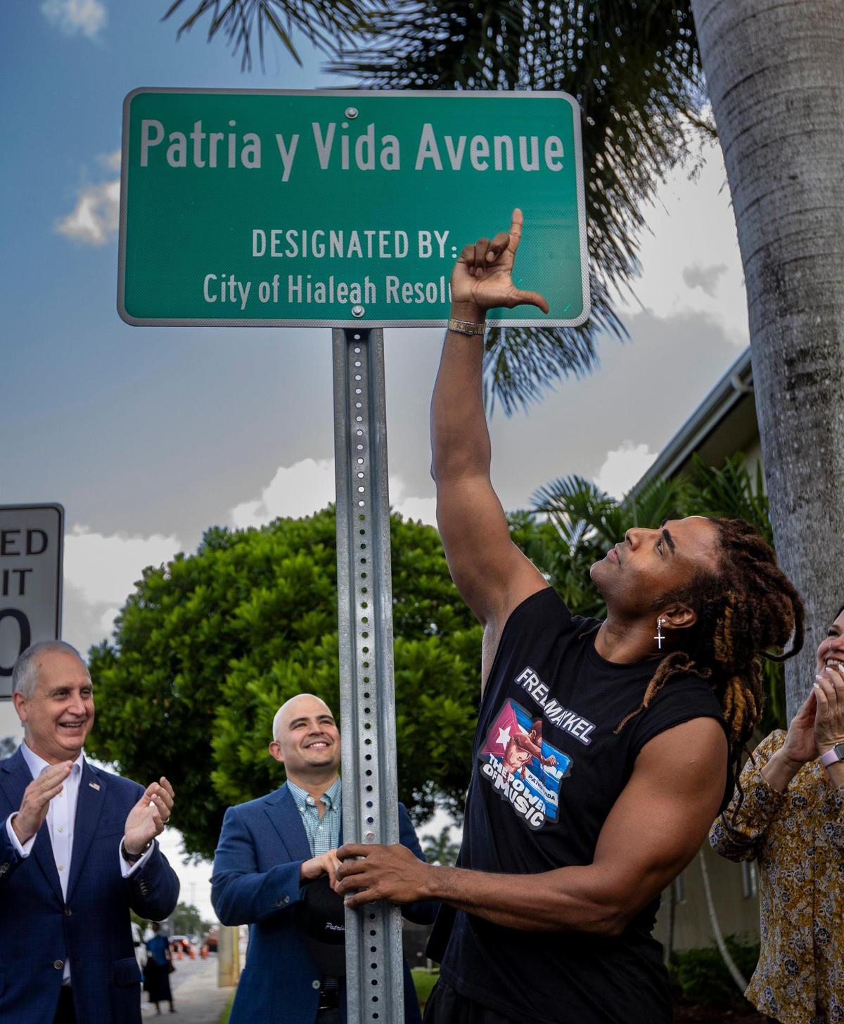 El cantante Yotuel Romero muestra la L de Libertad frente al nuevo letrero de la avenida Patria y Vida en Hialeah. Una sección de West 8th Ave en Hialeah pasó a llamarse Patria y Vida Avenue en conmemoración de las protestas de 2021 en Cuba. Hialeah, Florida - 10 de julio de 2023 -