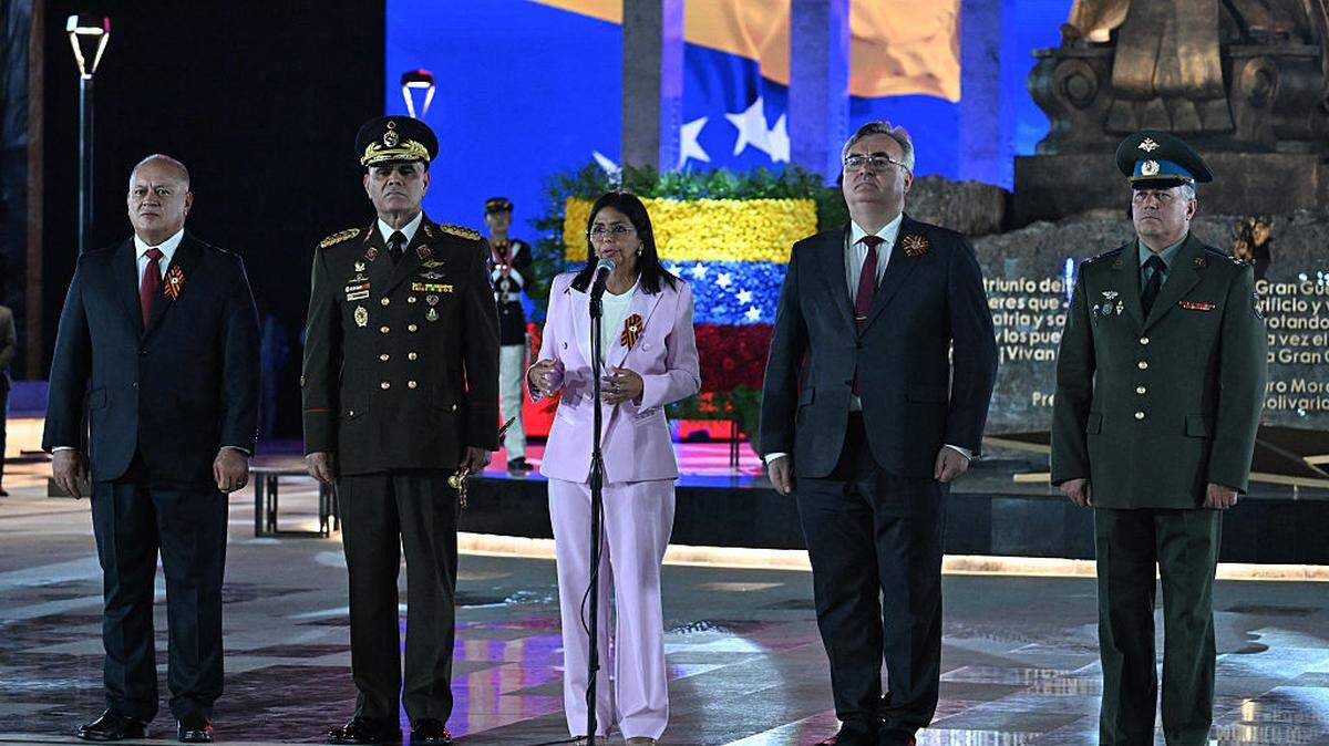 La entonces vicepresidenta de Venezuela, Delcy Rodríguez (c), habla junto al ministro del Interior de Venezuela, Diosdado Cabello (izq.), el ministro de Defensa venezolano, general Vladimir Padrino López (2.º desde la izq.), y el embajador ruso, Sergey Mélik-Bagdasárov (2.º desde la der.), durante un desfile militar en la inauguración de la Plaza de la Victoria, conmemorando el 80.º aniversario de la victoria de la Unión Soviética sobre la Alemania nazi en la Segunda Guerra Mundial (SGM), en Caracas, el 13 de mayo de 2025. 