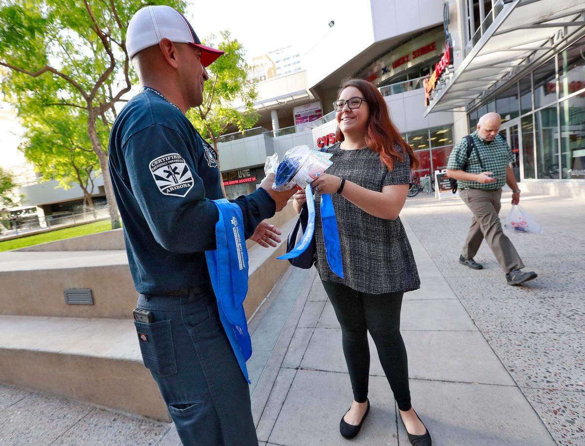 El bombero de Phoenix, Juan Rodriguez, reparte una pañoleta de enfriamiento a  Arielle Thomas quien va caminando a su trabajo.