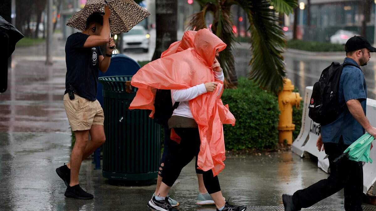 Peatones intentan mantenerse secos mientras la lluvia inunda la zona el 15 de noviembre de 2023 en Miami Beach, Florida.