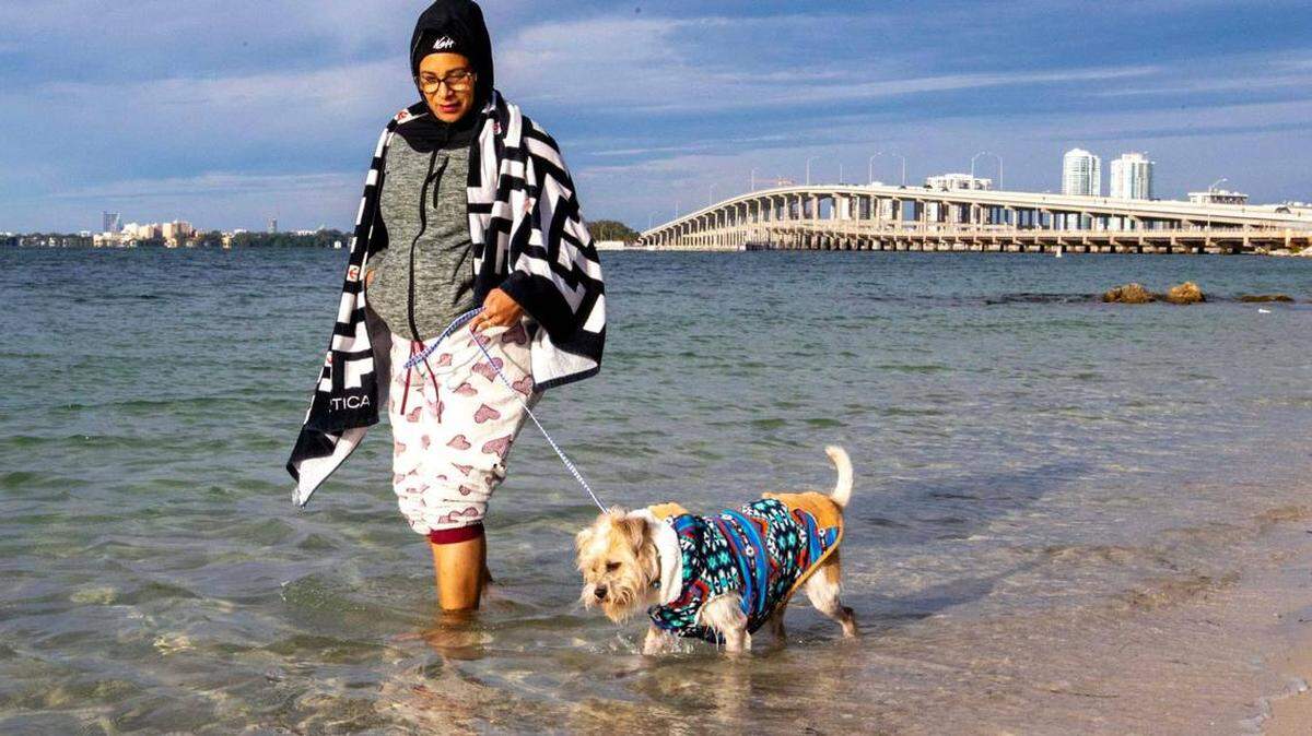 Muy abrigada, Kristal García, de 48 años, pasea su perro, Jay, por el agua del Parque Hobie Island Beach, en Key Biscayne, Florida, el sábado 24 de diciembre de 2022.