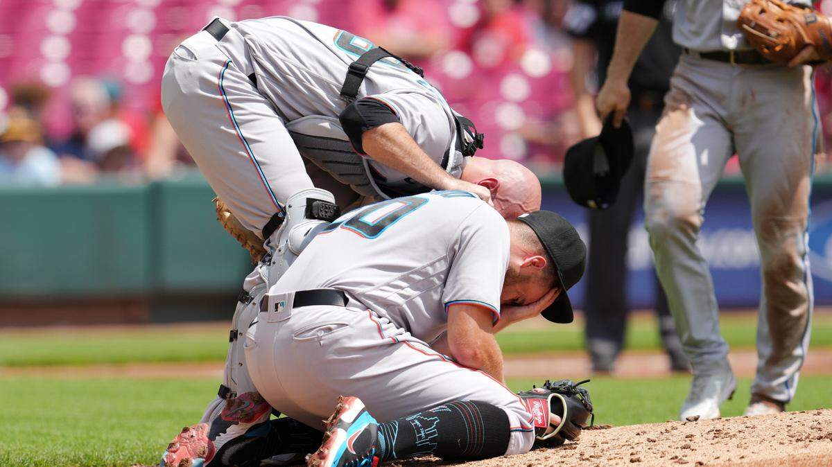 El receptor de los Marlins Jacob Stallings auxilia al lanzador abridor Dan Castano, quien fue golpeado en la frente por una línea que bateó el colombiano Donovan Solano, en la primera entrada del partido en Cincinnati, el jueves 28 de julio de 2022.
