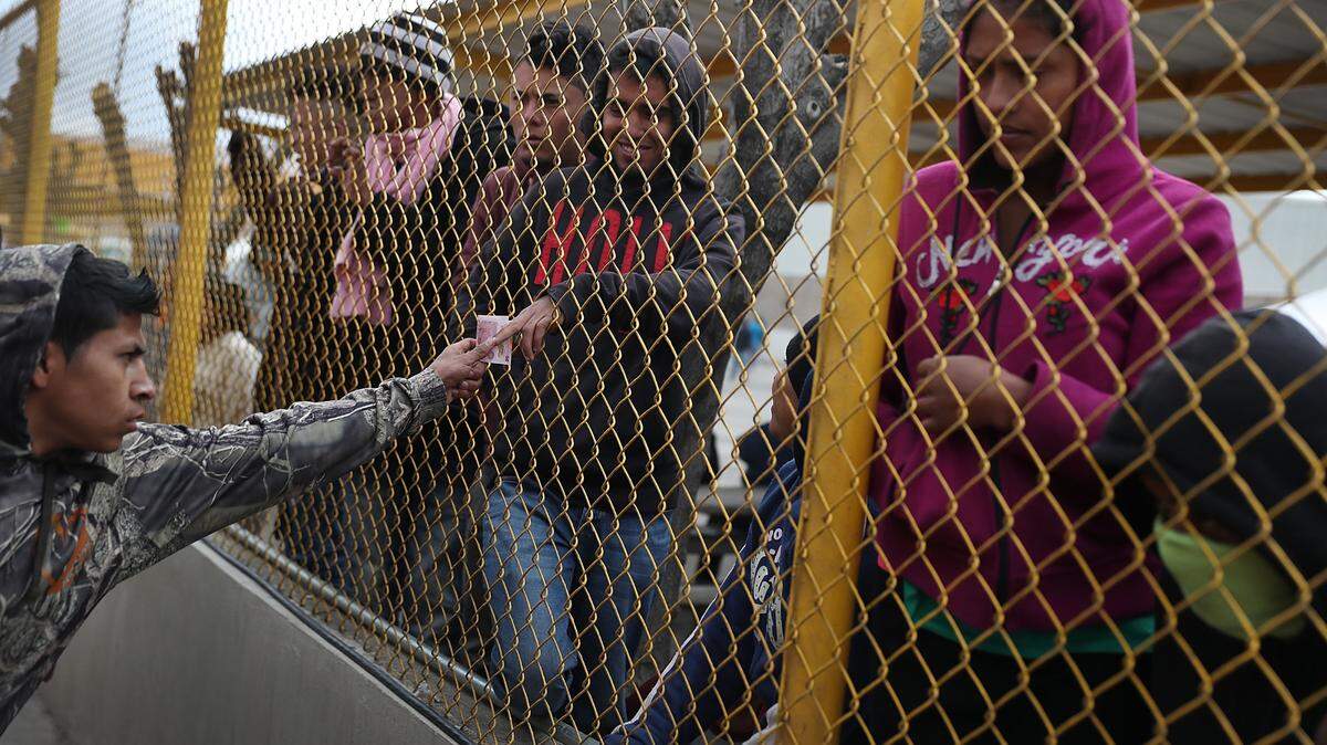 Un migrante pasa dinero para comprar café y otras golosinas de un vendedor a través de una cerca mientras se hospeda en un albergue para migrantes mientras esperan para solicitar asilo en los Estados Unidos el 9 de febrero de 2019 en Piedras Negras, México. El albergue cuenta con aproximadamente 2,000 migrantes de Honduras, Guatemala y El Salvador, donde se los atiende con alimentos, refugio y atención médica. (Getty Images / Joe Raedle)