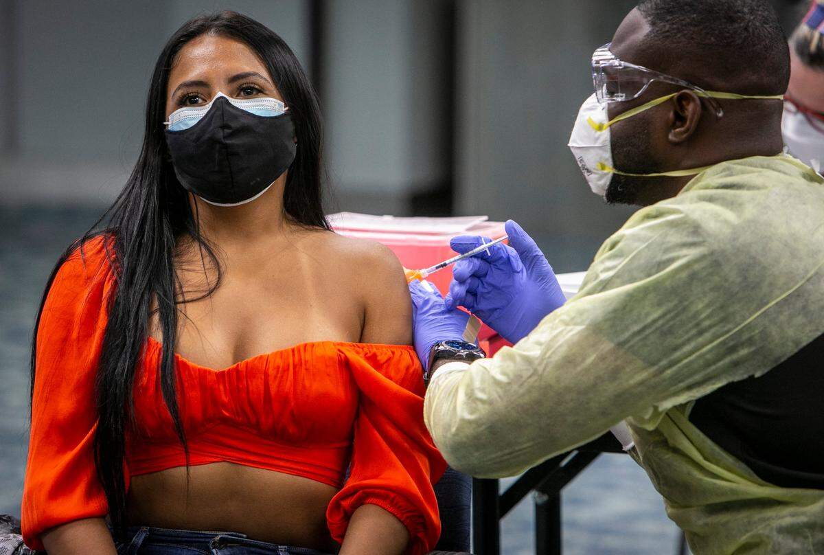 Miami, Florida, May 9 2021 - Sigrey Gonzalez Flores (left) from Costa Rica, gets her Pfizer vaccine at the pop up vaccination site in Concourse D in the 4th floor auditorium at Miami International Airport. The vaccines will be available to airport employees, their family and friends, and travelers living or working in Florida starting Monday, May 9, 2021, from 8 a.m. to 5 p.m. and through May 14, then June 1 through 4, and June 7, according to airport officials. There will be two locations at MIA, one will be a drive through, while the other will be in Concourse D in the 4th Floor Auditorium. The drive through will be set up at 75 Bus Road, Miami, FL 33102 (MIA taxi overflow lot).