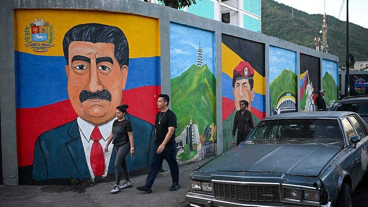 People walk in front of a mural depicting Venezuela's President Nicolas Maduro in Caracas on November 13, 2025. (Photo by Federico PARRA / AFP) (Photo by FEDERICO PARRA/AFP via Getty Images)