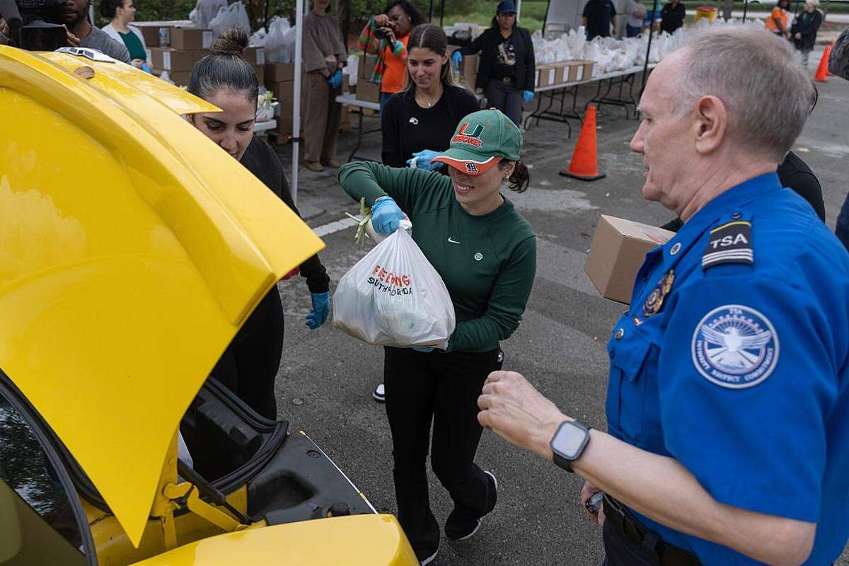 Laritza Puentes y otros voluntarios de Feeding South Florida colocan bolsas de alimentos en el vehículo de un empleado gubernamental el 17 de marzo de 2026 en Miami, Florida. La distribución de alimentos se llevó a cabo en el estacionamiento para empleados del Aeropuerto Internacional de Miami.