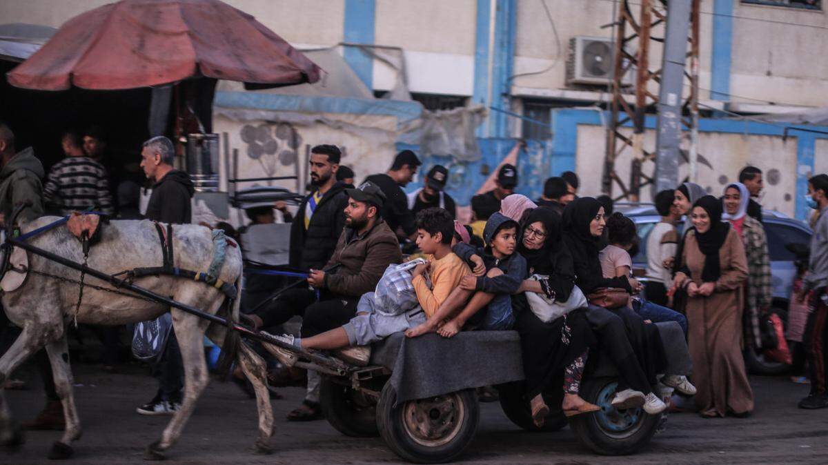Decenas de palestinos, unos en carreta, otros a pie, pasan frente al hospital Nasser y una escuela administrada por las Naciones Unidas, en Khan Yunis, Franja de Gaza, el jueves 30 de noviembre de 2023.