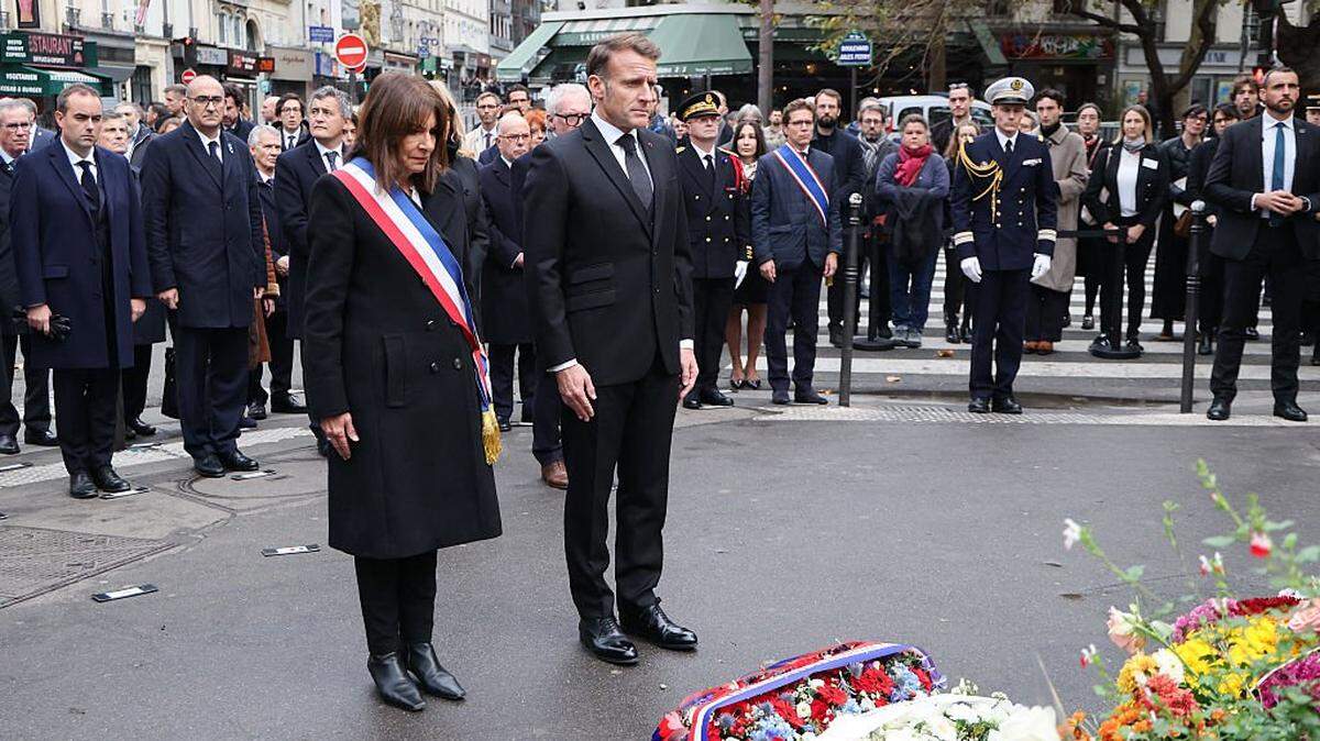 France's Prime Minister Sebastien Lecornu (L), France's Interior Minister Laurent Nunez (2nd-L), France's Justice Minister Gerald Darmanin (3rd-L) stand next to Paris' mayor Anne Hidalgo (C-L) and France's President Emmanuel Macron (C-R) as they pay tribute to victims at intersection of Faubourg du Temple and Boulevard Jules Ferry near "La Bonne Biere" cafe in Paris on November 13, 2025, during ceremonies across Paris marking a decade since the terror attacks of November 13, 2015 in which 130 civilians were killed. (Photo by Ludovic MARIN / POOL / AFP) (Photo by LUDOVIC MARIN/POOL/AFP via Getty Images)