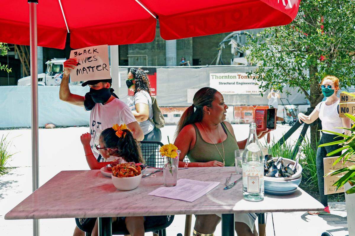 Tanya Maddison y su hija Cydney disfrutan de un almuerzo en North Italia mientras un grupo de manifestantes pasan por The Shops at Mary Brickell Village en el barrio de Brickell en Miami, el sábado 13 de junio de 2020.