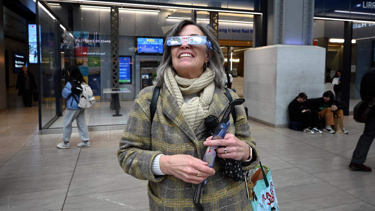 Beth Perinelli prueba unos lentes para eclipse solares que recibió gratis en la estación de trenes de la Autoridad Metropolitana del Transporte (MTA, por sus siglas en inglés), en Moynihan Train Hall, Nueva York, el lunes 1 de abril de 2024.