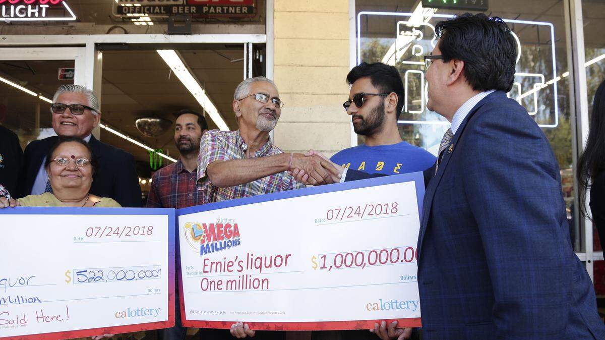 Kewal Sachdev, left, shakes Russ Lopez’ hand while receiving a symbolic check for $1 million outside his store Ernie’s Liquors in San Jose, Calif., on Wednesday, July 25, 2018. Sachdev’s store sold the winning Mega Millions lottery ticket worth $543 million. (Maritza Cruz/Bay Area News Group/TNS)