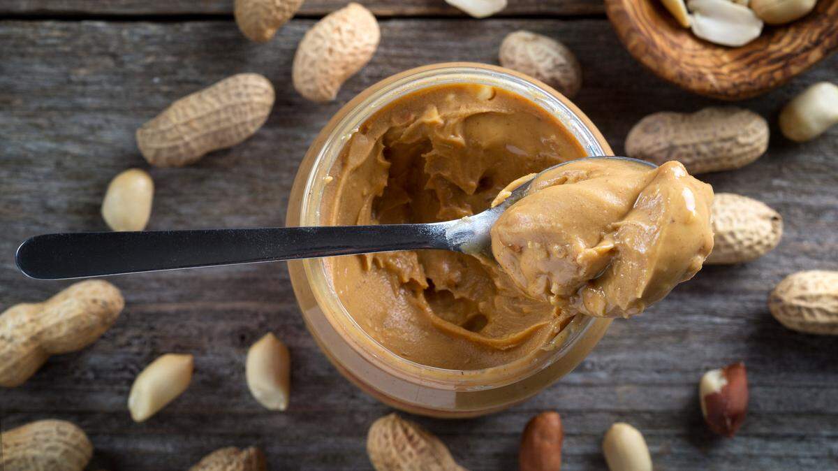 Spoon and pot of peanut butter on wooden background - top view