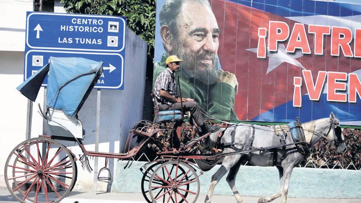 Un hombre conduce su carruaje tirado por un caballo frente a una imagen del ex gobernante Fidel Castro en Bayamo.