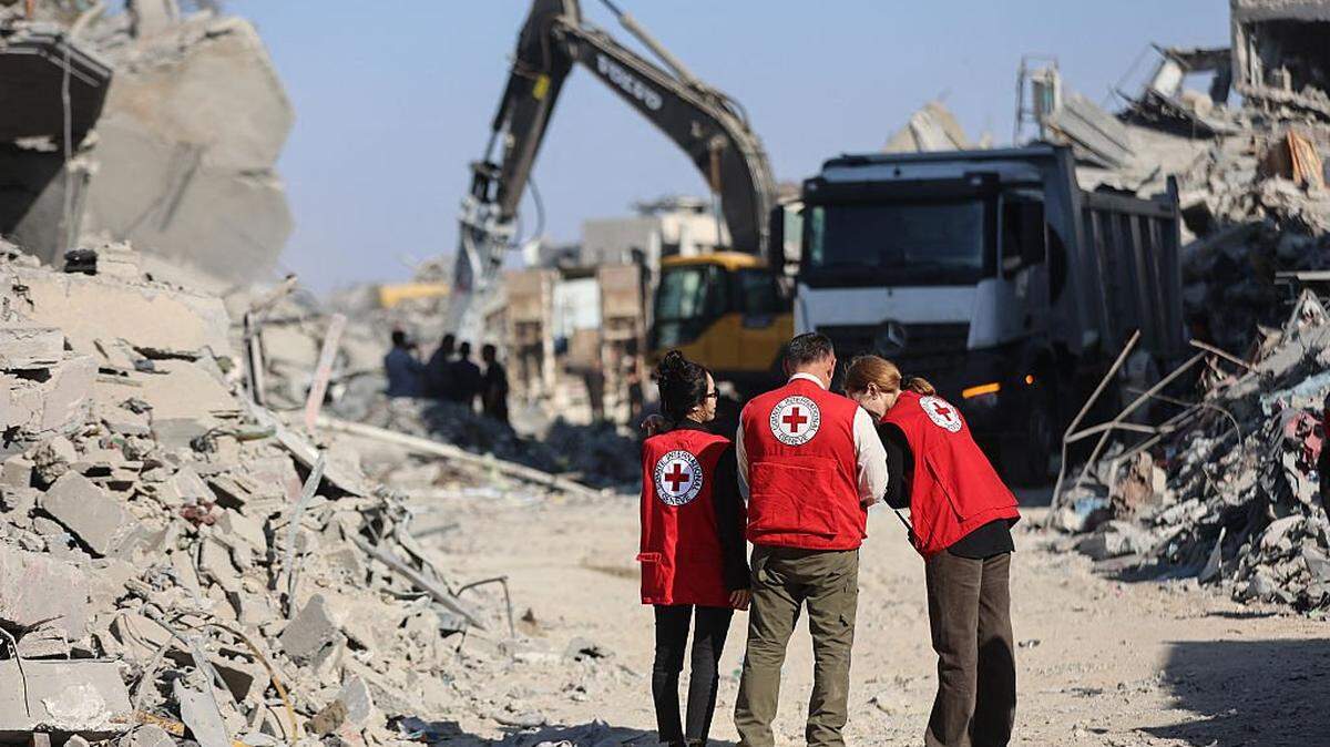 Members of the Red Cross stand amid the rubble of destroyed buildings as heavy machinery operates in the al-Tuffah neighbourhood of Gaza City on October 27, 2025. The families of Israeli hostages on October 27 demanded that the next steps in the US-brokered Gaza ceasefire be put on hold until Hamas returns the remaining bodies of dead captives. In the past two days, Egypt has sent recovery crews and heavy earth-moving equipment into Gaza, with Israeli approval, to help with the recovery operation of the bodies of Israeli hostages. (Photo by Omar AL-QATTAA / AFP) (Photo by OMAR AL-QATTAA/AFP via Getty Images)