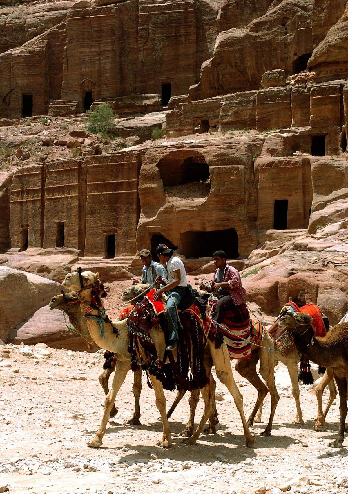 Grupo de beduinos en camello delante de algunas tumbas en el enclave arqueológico de Petra, en Jordania.