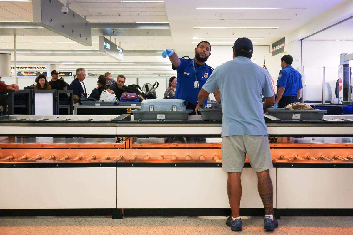 Un agente de la TSA indica a un viajero que coloque sus pertenencias personales dentro de una cesta en el nuevo sistema automatizado de devolución de cestas en el puesto de control 2 del Aeropuerto Internacional de Miami el martes 25 de noviembre en Miami, Florida.