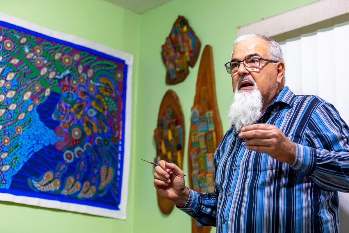 El artista cubano Zaplaflora Jesús Torres habla sobre su trabajo mientras pinta en el estudio de su casa en Hialeah, Florida, el jueves 17 de noviembre de 2022. A su espalda se exhiben algunas de sus obras coloniales, de sus primeros años como artista junto con uno de sus más recientes cuadro “El origen amazónico”, inspirado en la naturaleza