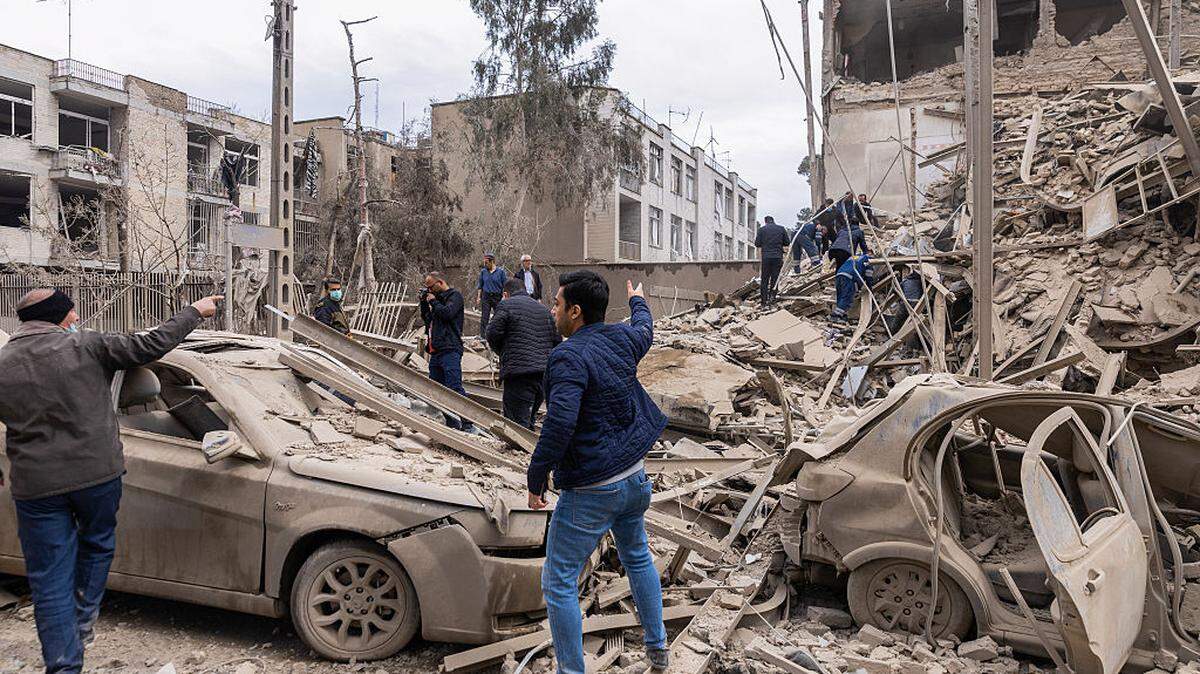 Varias personas reaccionan mientras los equipos de emergencia buscan a personas atrapadas entre los escombros tras el ataque a un edificio residencial el lunes, 16 de marzo de 2026, en el centro de Teherán, Irán.