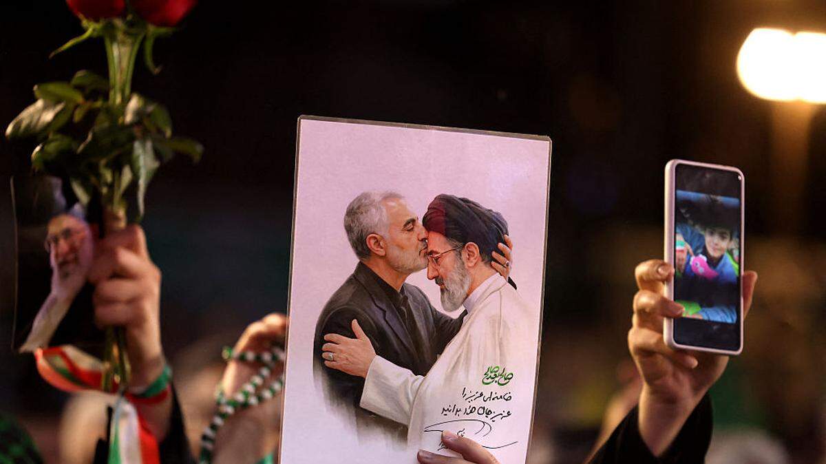 Un hombre sostiene una pancarta con fotografías del líder supremo de Irán, el ayatolá Mojtaba Khamenei, junto al oficial militar asesinado Qasem Soleimani, mientras asiste a la ceremonia de despedida de la selección nacional de fútbol de Irán antes de su partida hacia la Copa Mundial de la FIFA 2026, en Teherán, el miércoles 13 de mayo de 2026.