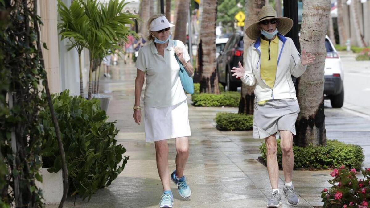 Robin Pickett y Peggy Mejia, usan máscaras protectoras mientras caminan por Worth Ave. durante la nueva pandemia de coronavirus, el lunes 11 de mayo de 2020, en Palm Beach, Florida.