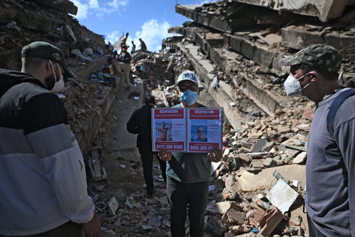 A man shows pictures of missing people amid the rubble at Los Cocos beach, in Caraballeda, La Guaira state, Venezuela, on July 1, 2026, following the June 24 twin earthquakes. Venezuelans, with help from around the world, were still searching on July 1, 2026 for survivors a week after massive earthquakes killed nearly 2,000 and left thousands unaccounted for. (Photo by Juan BARRETO / AFP via Getty Images)