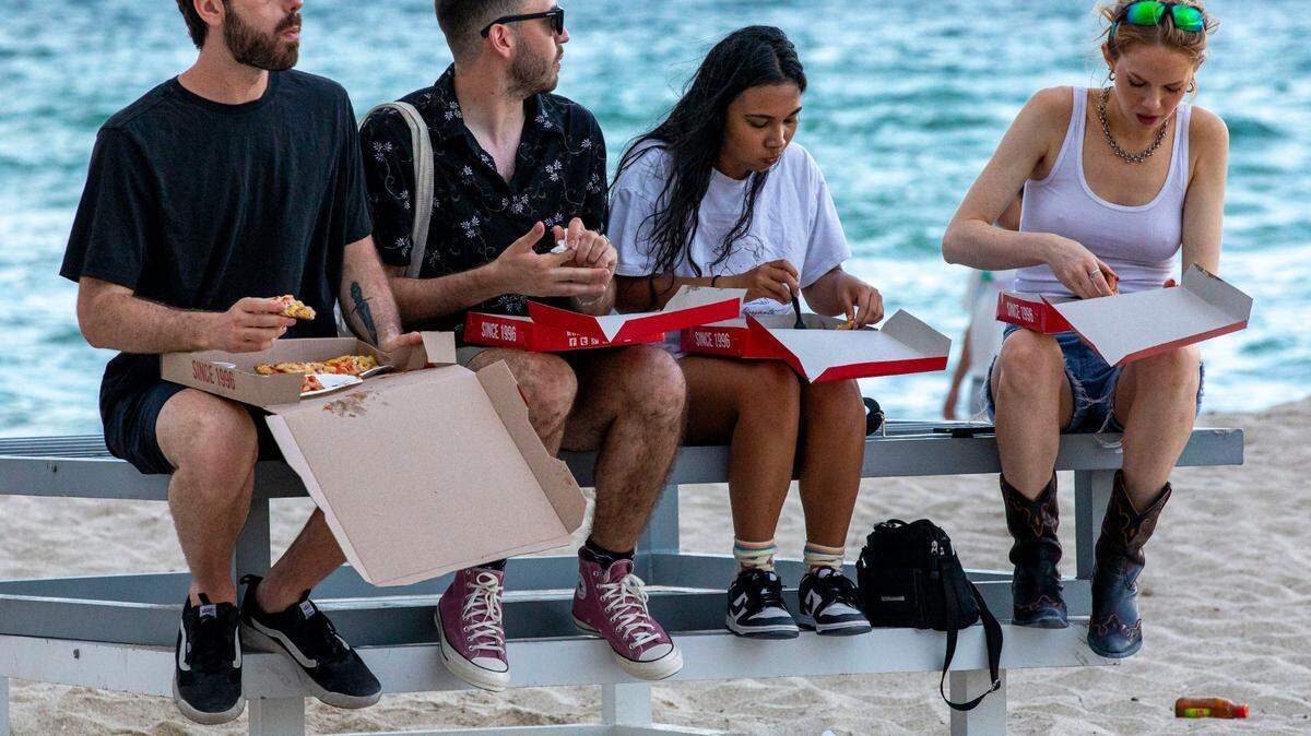 Un grupo de vacacionistas de Nueva York come pizza en la playa durante el segundo día del fin de semana del Día de los Caídos en Miami Beach, Florida, el sábado 28 de mayo de 2022.