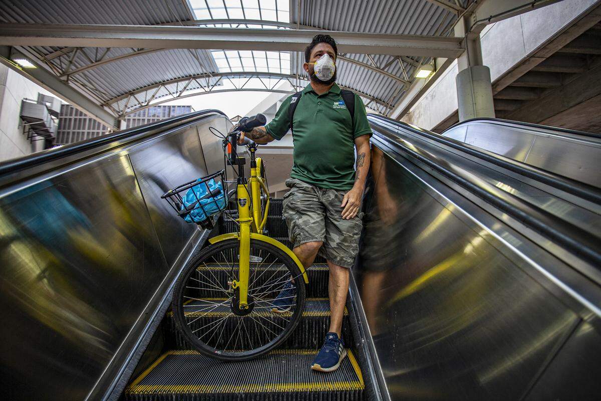 Andrew Cendan, de 42 años, viaja en la escalera mecánica junto con su bicicleta mientras viaja al trabajo en Metrorail con una máscara protectora durante la pandemia COVID-19 en el centro de Miami el miércoles 1 de abril de 2020.