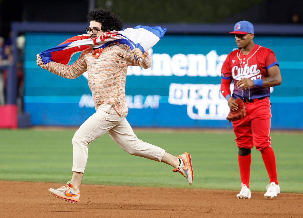 El manifestante y escritor Carlos Manuel Álvarez lleva una bandera cubana con las palabras ‘Patria y Vida’ y corre en el campo mientras el jugador de cuadro cubano Andy Ibáñez (77) observa durante el partido entre Estados Unidos y Cuba, en la semifinal del Clásico Mundial de Béisbol celebrada en el LoanDepot Park en Miami, Florida, el 19 de marzo de 2023.