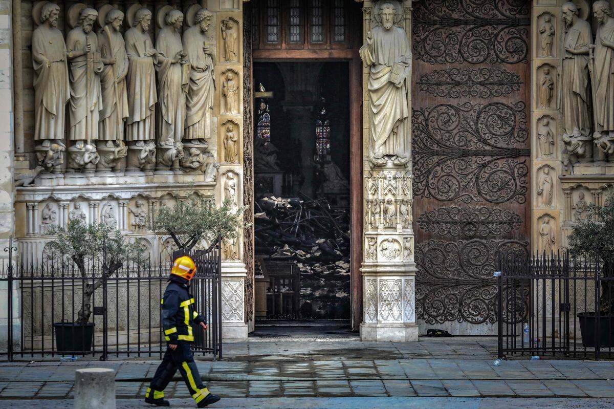 Un bombero camina junto a una puerta donde puede verse el interior de la catedral Notre Dame de París el martes 16 de abril del 2019, un día después del incendio.