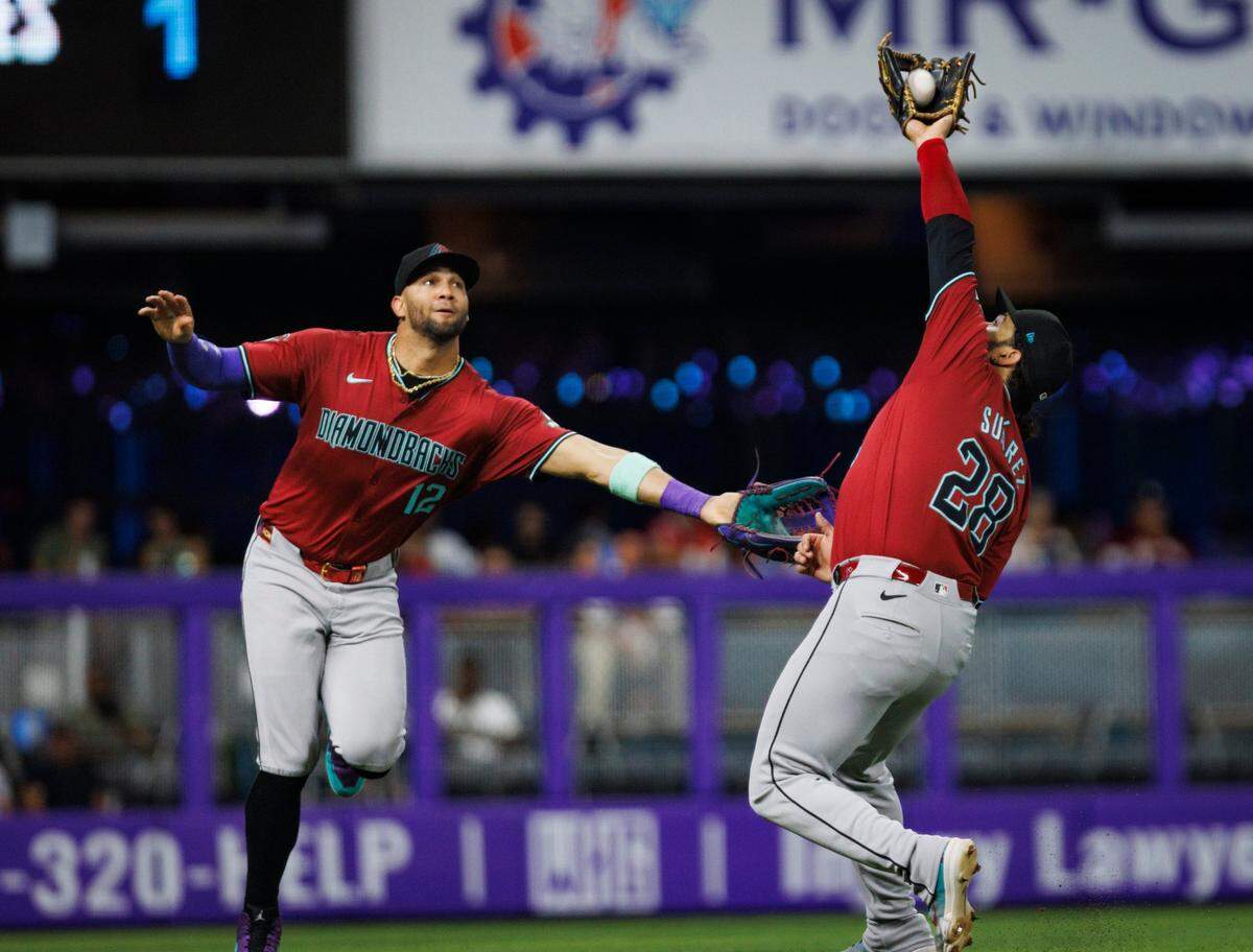 El jardinero de los Diamondbacks de Arizona Lourdes Gurriel Jr. (izq.) intenta atrapar la pelota que finalmente se lleva el tercera base Eugenio Suárez, en una jugada en el segundo inning del partido contra los Marlins, celebrado el 19 de agosto de 2024 en Miami.