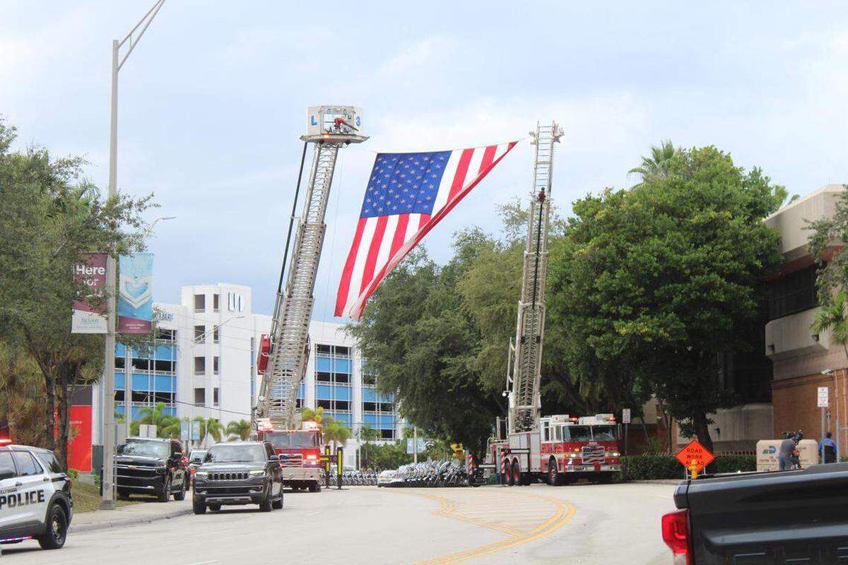Una gran bandera estadounidense cuelga de las escaleras de dos camiones del cuerpo de bomberos de Miami-Dade estacionados en el Hospital Jackson Memorial, el martes 28 de octubre de 2025, en honor al oficial de la Policía de Miami Beach David Cajuso, quien murió horas antes en un accidente de motocicleta en la autopista I-75. Devoun Cetoute — dcetoute@miamiherald.com