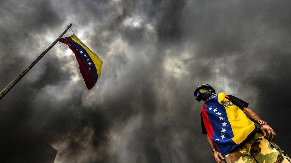 Un manifestante se encuentra junto a una bandera nacional durante una protesta de la oposición que bloquea la carretera Francisco Fajardo en Caracas el 27 de mayo de 2017.