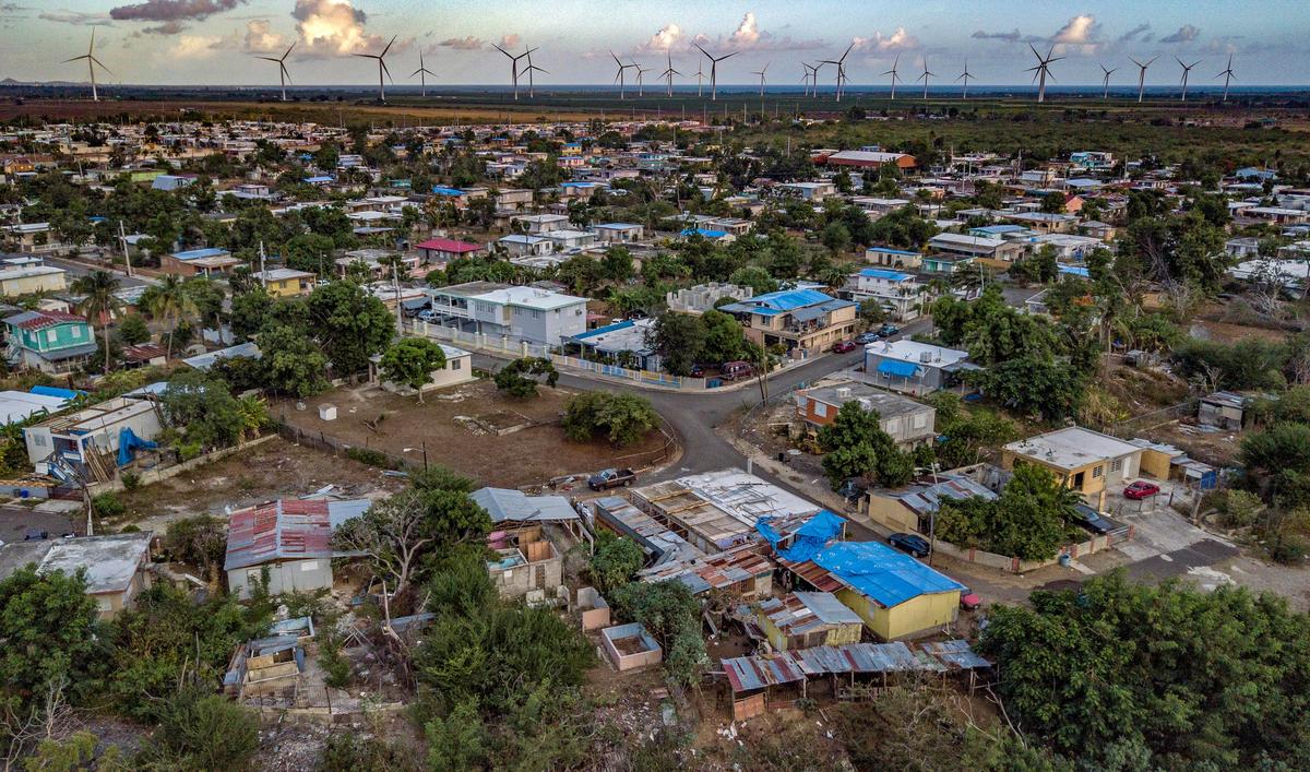 Un año después de que el huracán María azotara la isla, se ven lonas azules que cubren los techos de las casas cerca de Coamo, Puerto Rico. A lo lejos se encuentran las turbinas eólicas que ahora están en funcionamiento.