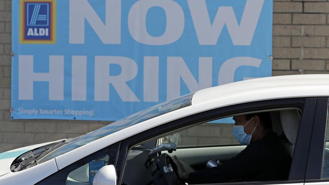 A worker waits in front of a hiring sign at an Aldi grocery store.