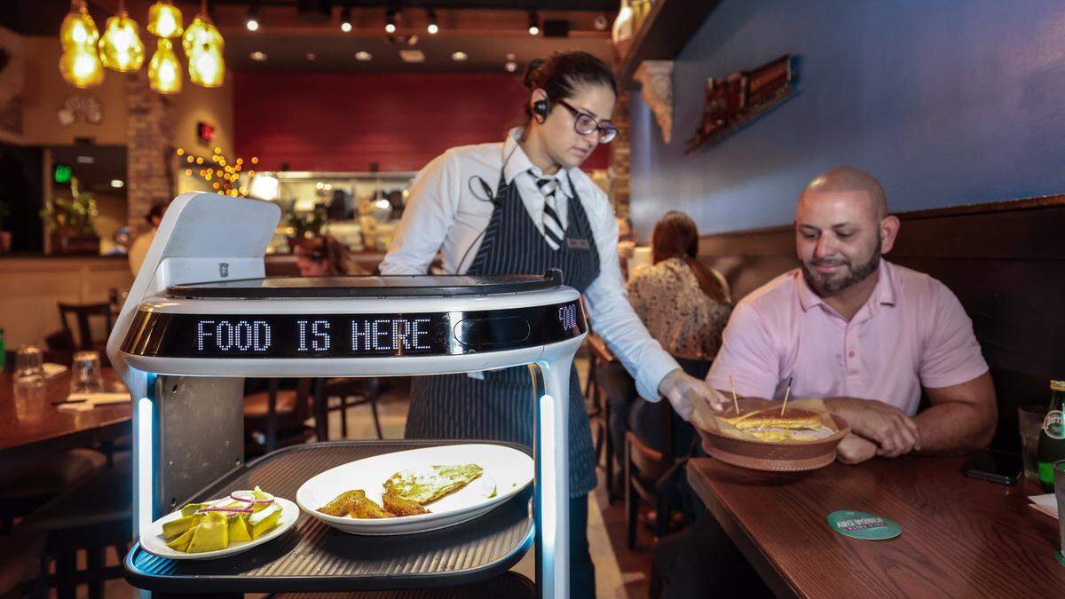 La mesera Cecille Artigas atiende a Alex Bustamante desde un carrito de comida robotizado en el restaurante Sergio’s de Kendall. 