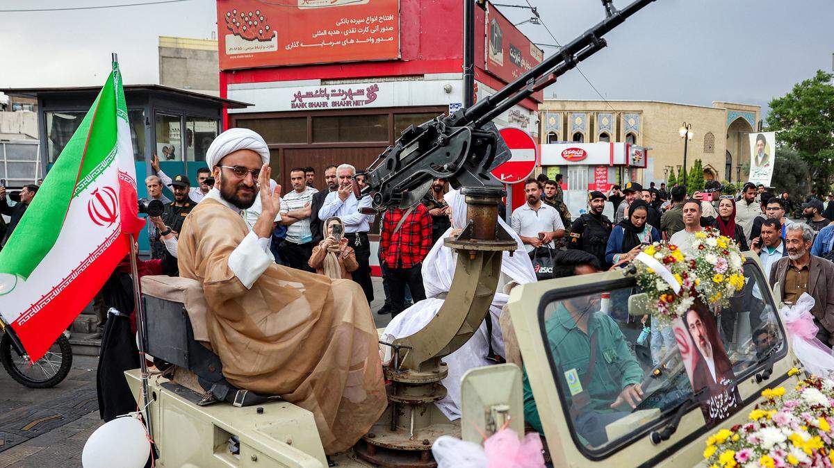Un clérigo musulmán chiita saluda mientras viaja como novio junto a su esposa en un jeep militar al llegar a una ceremonia pública de bodas masivas en la plaza Imam Hossein, en Teherán, el 18 de mayo de 2026.