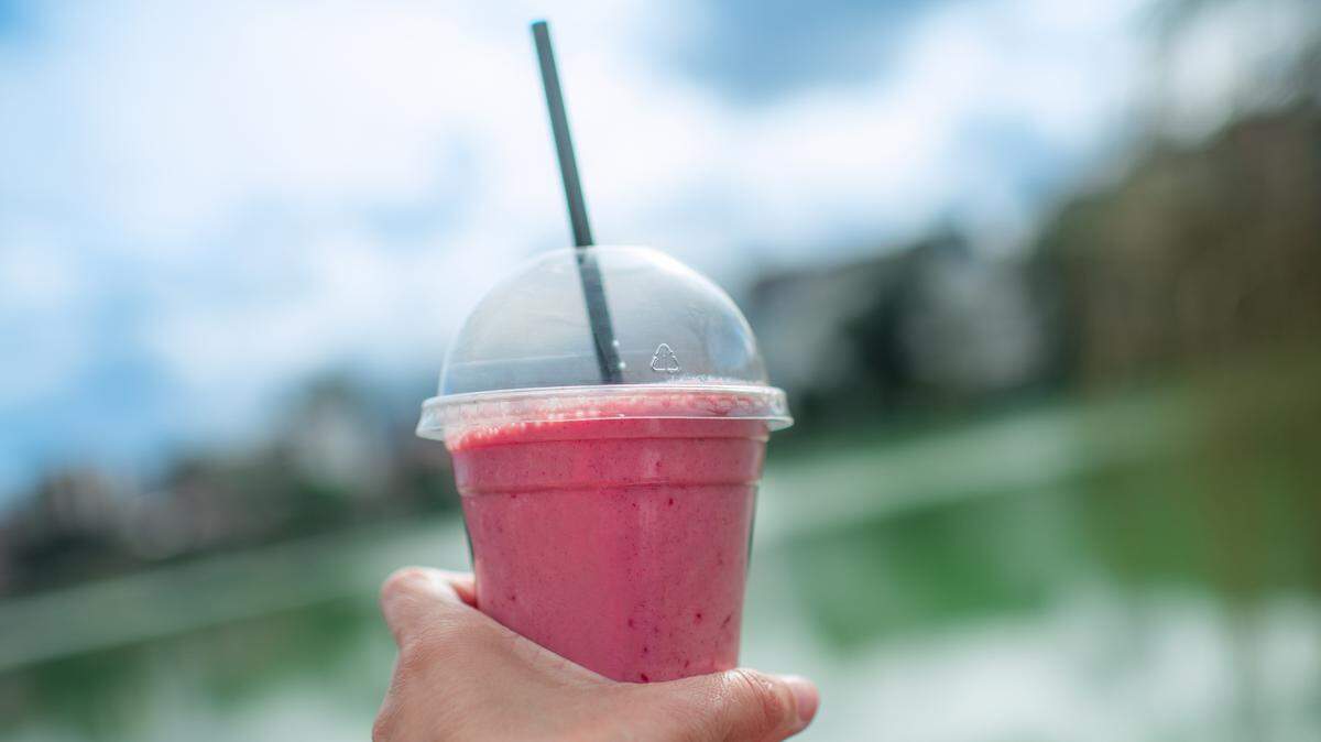 Smoothy in  plastic take away cup in a woman’s hand over city park background