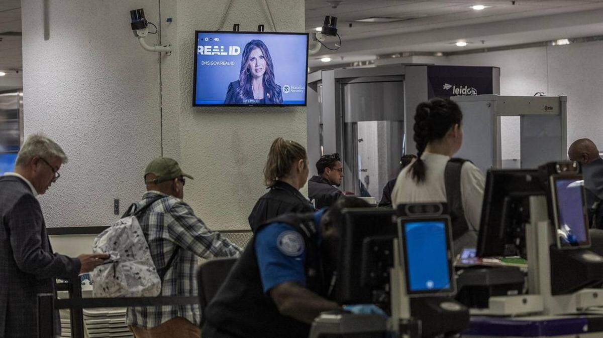 Pasajeros pasan por un puesto de control mientras se muestra información sobre la tarjeta REAL ID en una pantalla en el Aeropuerto Internacional de Miami el miércoles 7 de mayo de 2025.