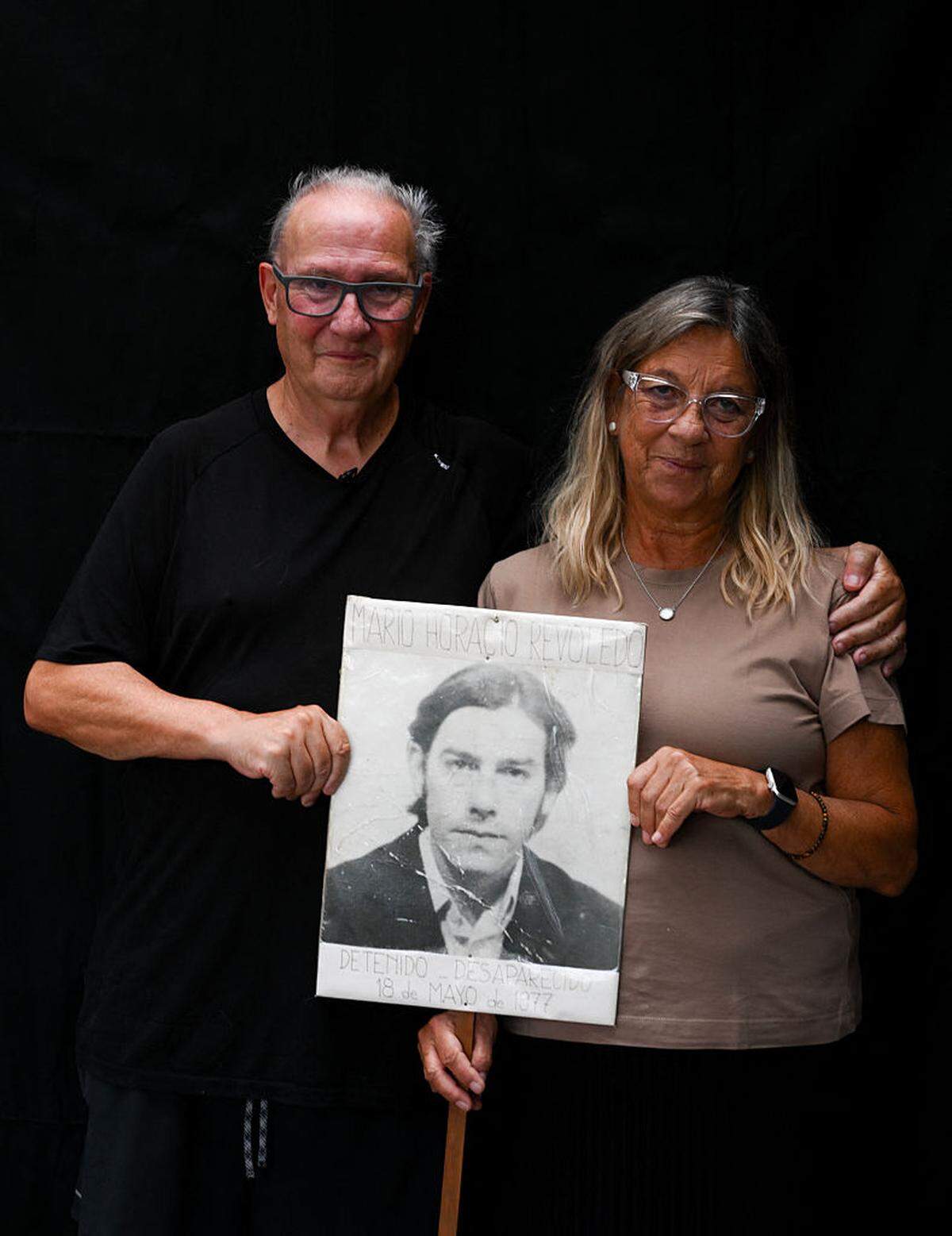 Pablo Díaz (izq.), de 67 años —quien fue secuestrado en La Plata el 16 de septiembre de 1976, durante la dictadura militar (1976-1983)—, posa junto a su esposa, Susana Bordoni, de 66 años, mientras sostienen un retrato de su primo Mario Horacio Revoledo, desaparecido durante la dictadura militar, al finalizar una entrevista con la AFP en La Plata, provincia de Buenos Aires, Argentina, el 13 de marzo de 2026.