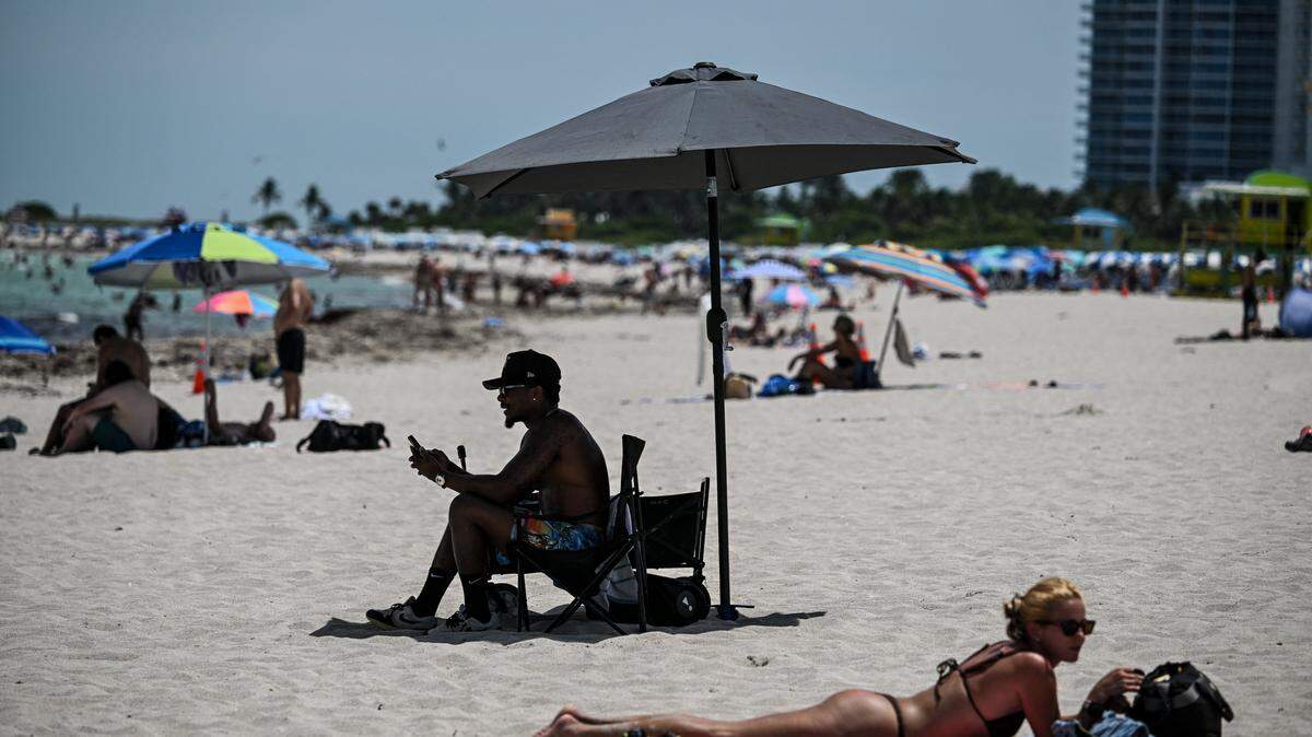 A man sits under a parasol as a woman sunbathes on a beach during a hot day in Miami Beach, Florida, on July 22, 2025. Some 85 million Americans from South Dakota to Texas and North Carolina to Florida are under National Weather Service extreme heat warnings, watches or advisories, with temperatures reaching 100 degrees Fahrenheit (38 degrees Celsius). (Photo by CHANDAN KHANNA / AFP) (Photo by CHANDAN KHANNA/AFP via Getty Images)          