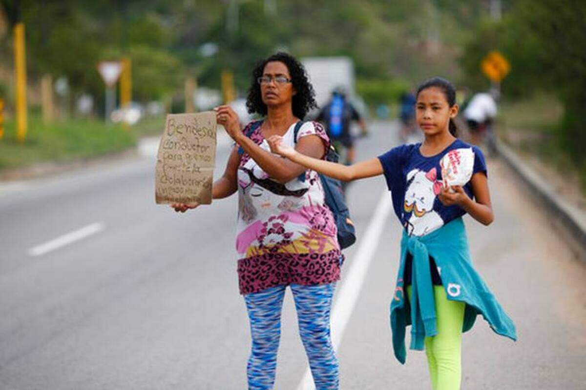 La venezolana Sandra Cádiz sostiene un letrero escrito a mano en que pide transporte, mientras su hija Angelis, de 10 años, la acompaña en la carretera que sale de Girón, Colombia, mientras las dos tratan de llegar a Perú, en una imagen de septiembre del 2018. Un número cada vez mayor de venezolanos, que no pueden darse el lujo de comprar ni siquiera un boleto de autobús, huyen a pie a otros países de la región.
