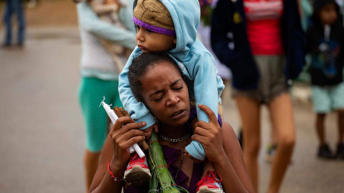 Una mujer aguanta el dolor de caminar de rodillas con su bebé en los hombros, durante una procesión hacia el santuario de San Lázaro, en El Rincon, Cuba, el domingo 17 de diciembre de 2023.