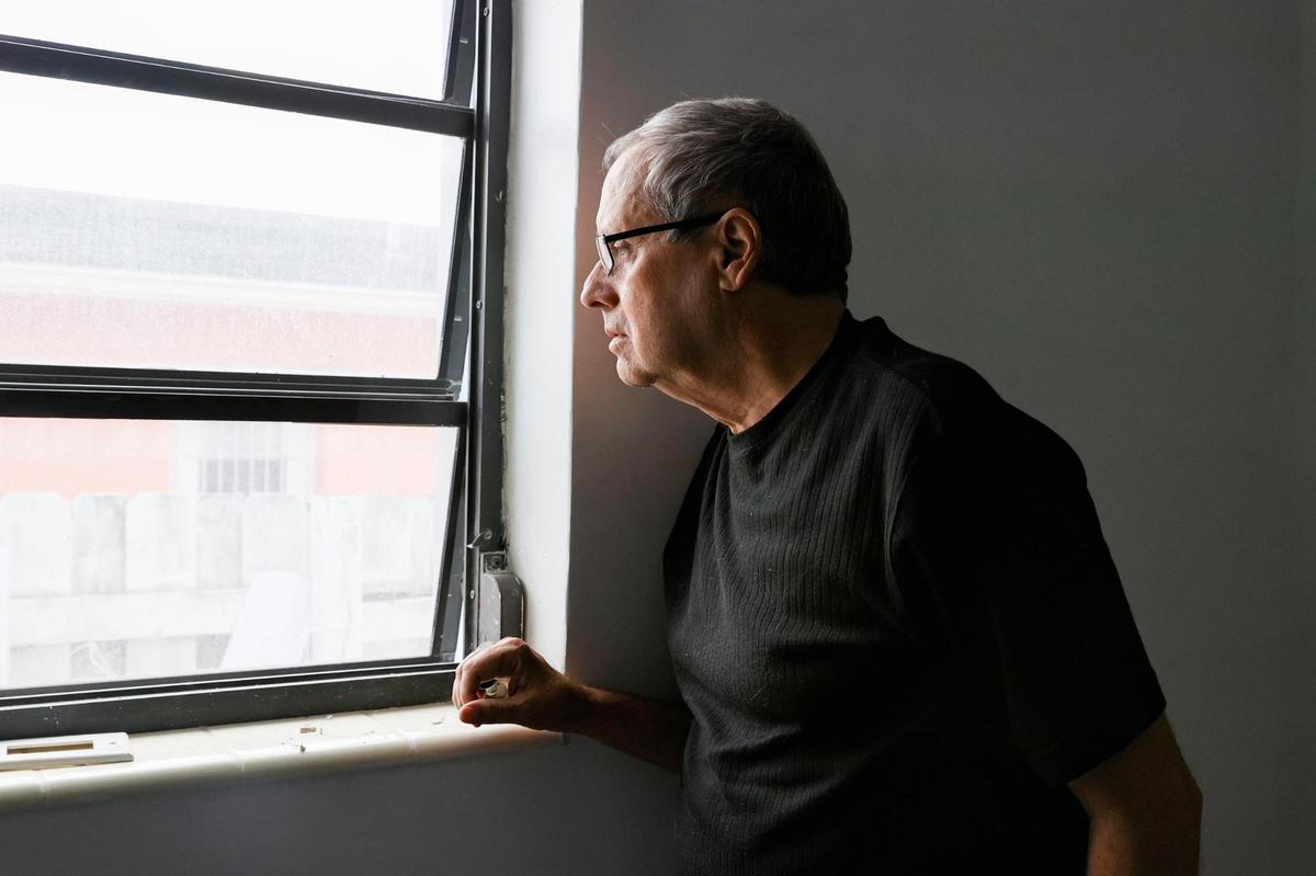 Writer Ismael Lorenzo, 76, looks through the window in his rented room at 4179 East Eighth Ct. in Hialeah, Florida, on Wednesday, Feb. 16, 2022. Lorenzo was evicted, by court order, from the apartment he rented in North Miami. When his contract began in September, he was not informed that the house was in foreclosure, and they kept the deposit money. He now has only been able to find a room in Hialeah for $1,100.