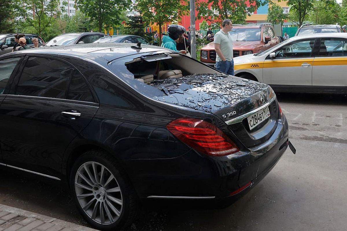 Residentes locales permanecen junto a un automóvil dañado en el patio de un edificio residencial tras un ataque aéreo en Krasnogorsk, región de Moscú, el 17 de mayo de 2026, en el marco del conflicto ruso-ucraniano en curso.