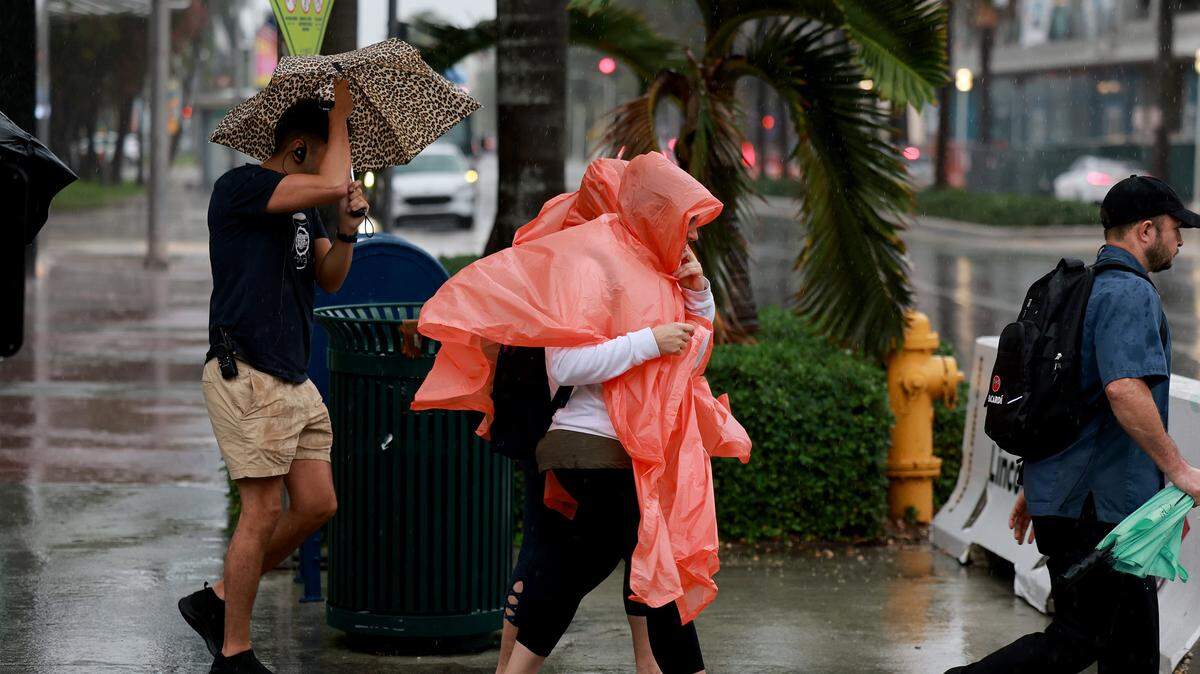 Peatones intentan mantenerse secos mientras la lluvia inunda la zona el 15 de noviembre de 2023 en Miami Beach, Florida.