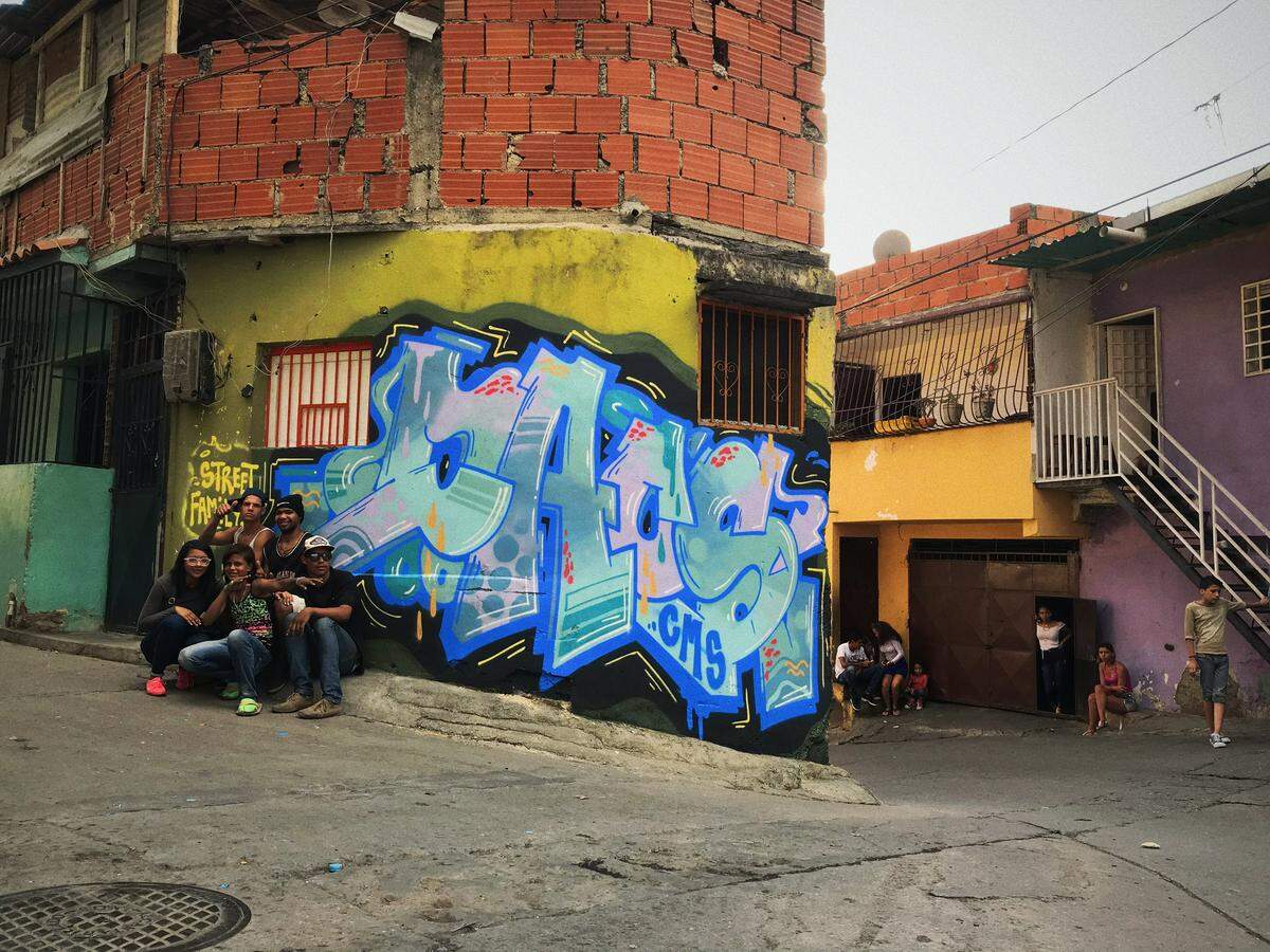 Vecinos del barrio del área de Petare posan junto a un grafiti de Daos243.