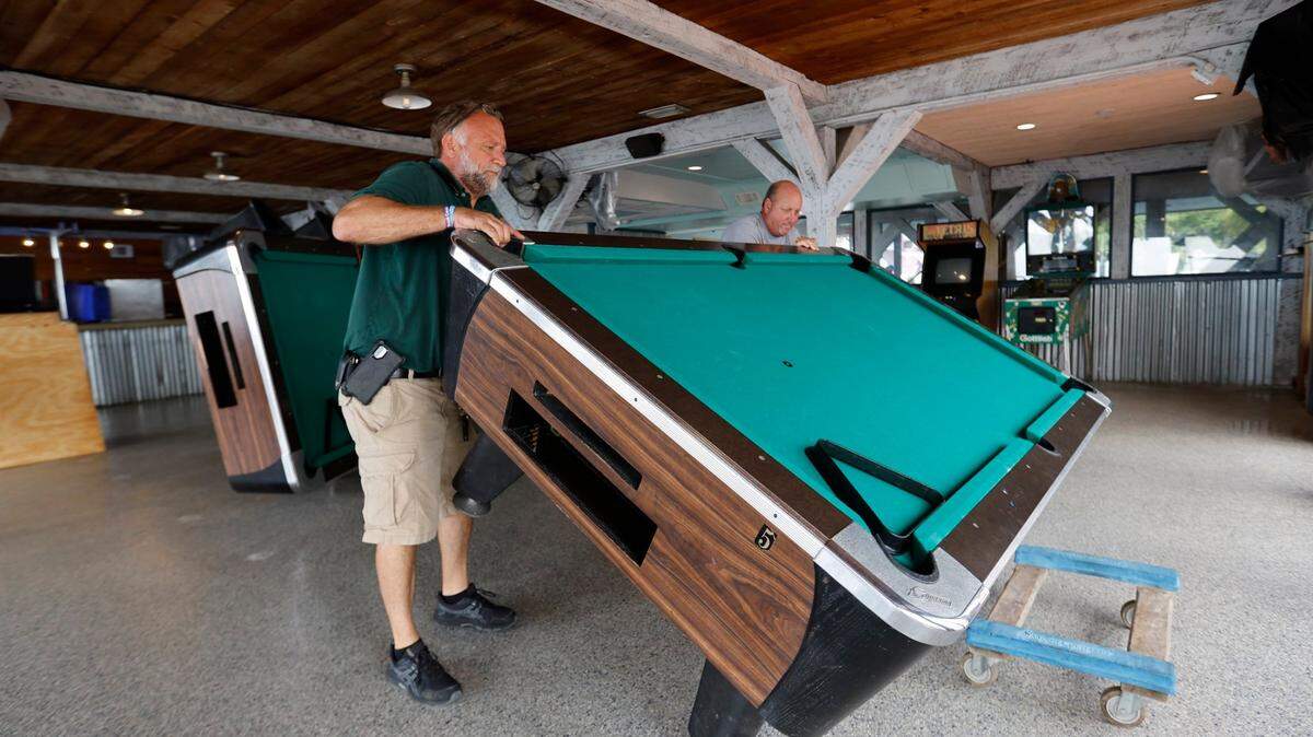Robert Bell (izq.) y Kurt Folsom mueven varias mesas de pool en su restaurante 83 West en Cedar Key, Florida, en preparación para el huracán Idalia, el martes 29 de agosto de 2023.