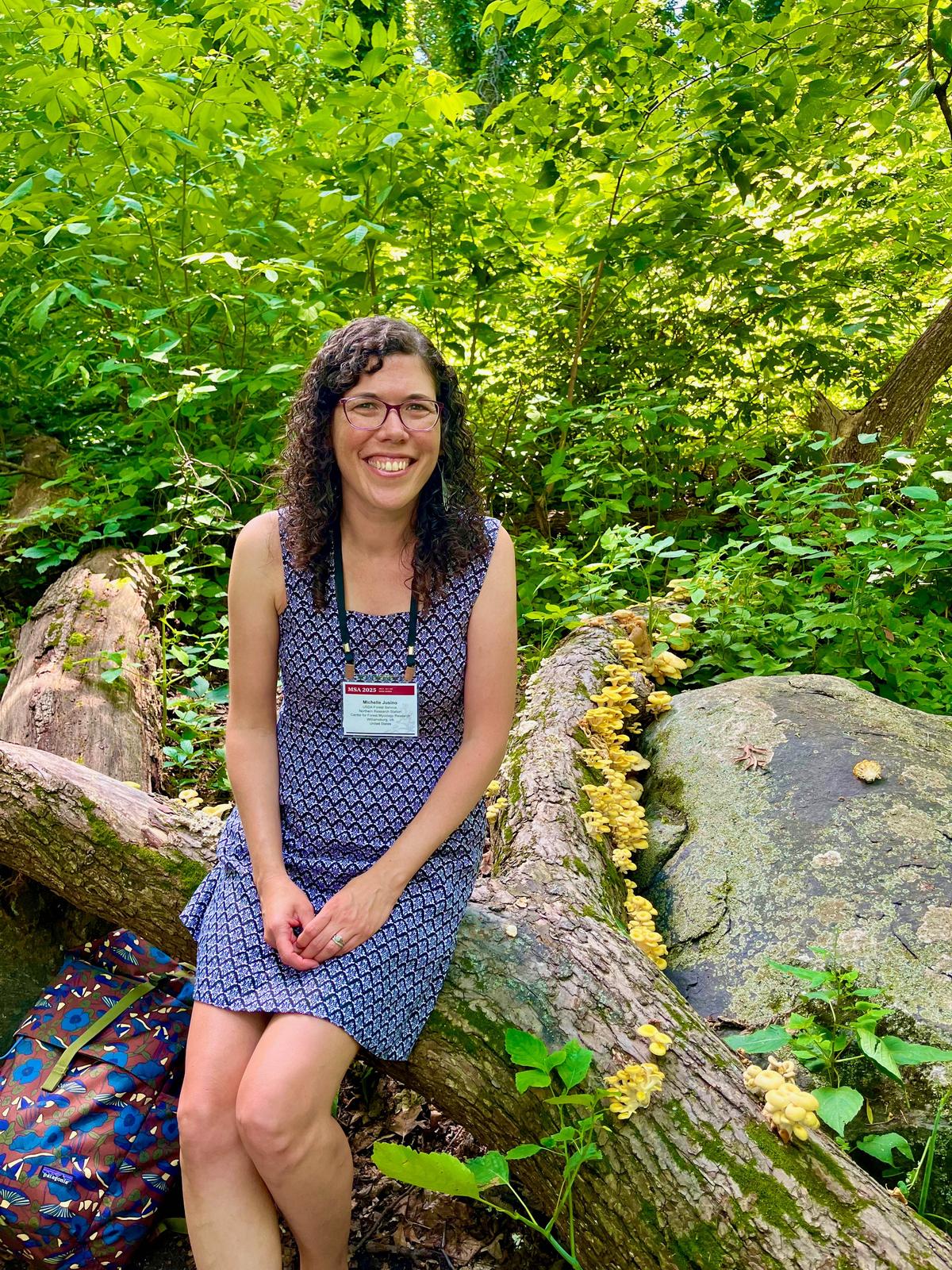 La Dra. Michelle Jusino sentada sobre un tronco cubierto de hongos ostra dorados (Pleurotus citrinopileatus) en Madison, Wisconsin.
