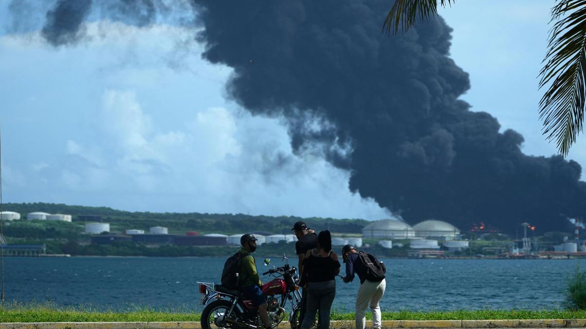 People look at a huge column of smoke rising from the Matanzas Supertanker Base, while firefighters and specialists work to extinguish a fire in Matanzas, Cuba, on Saturday, Aug. 6, 2022, that was caused by an electrical storm the day before. The fire and four associated explosions left more than 70 injured..